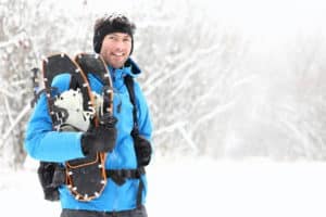 Winter snowshoeing. Young outdoorsman hiker standing smiling hap